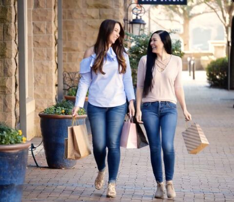 Two women walking on brick sidewalk with shopping bags.