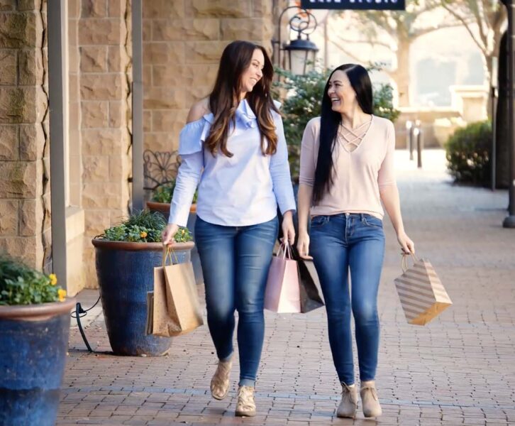 Two women walking on brick sidewalk with shopping bags.